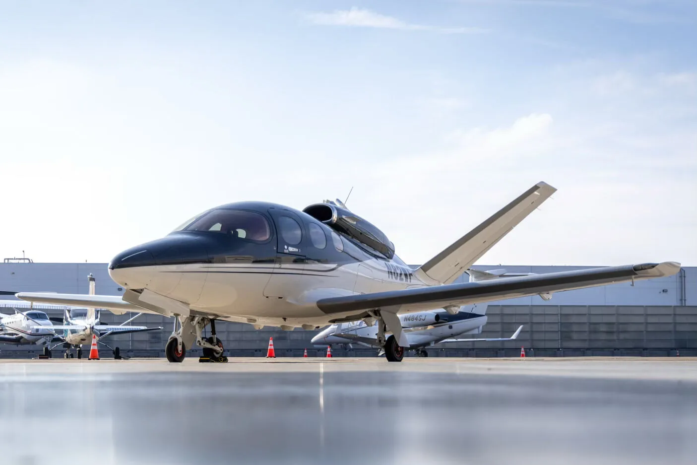 A low-angle three-quarter front view of a white and dark grey Cirrus Vision Jet (N82WF) parked on an airport tarmac.