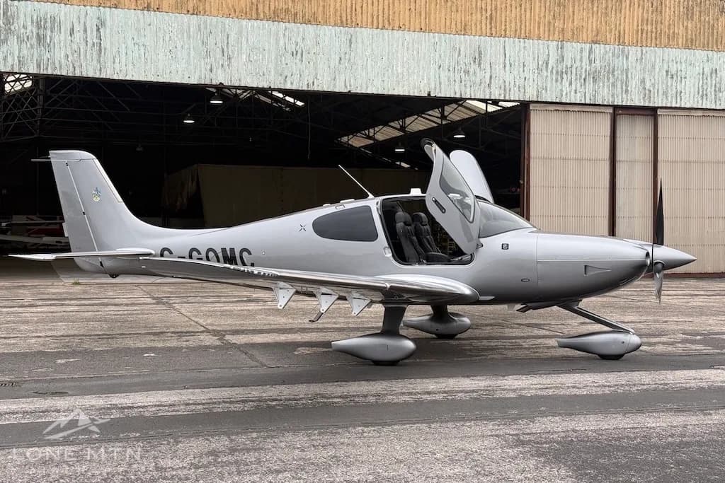A silver Cirrus SR22 aircraft with its gull-wing doors open, parked on an airfield.