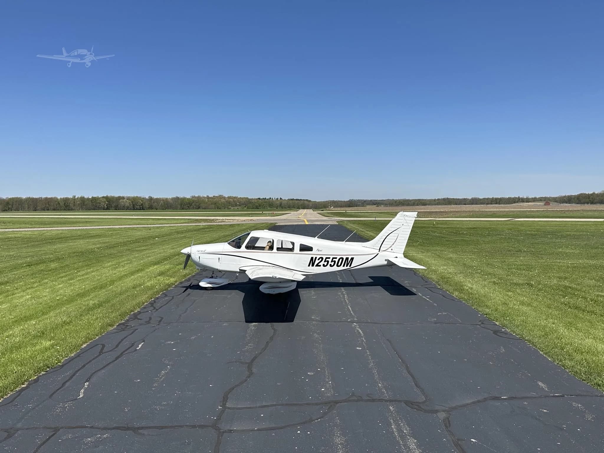 A white Piper Cherokee aircraft, N2550M, seen from a side angle on an asphalt runway, with a long view down the runway.