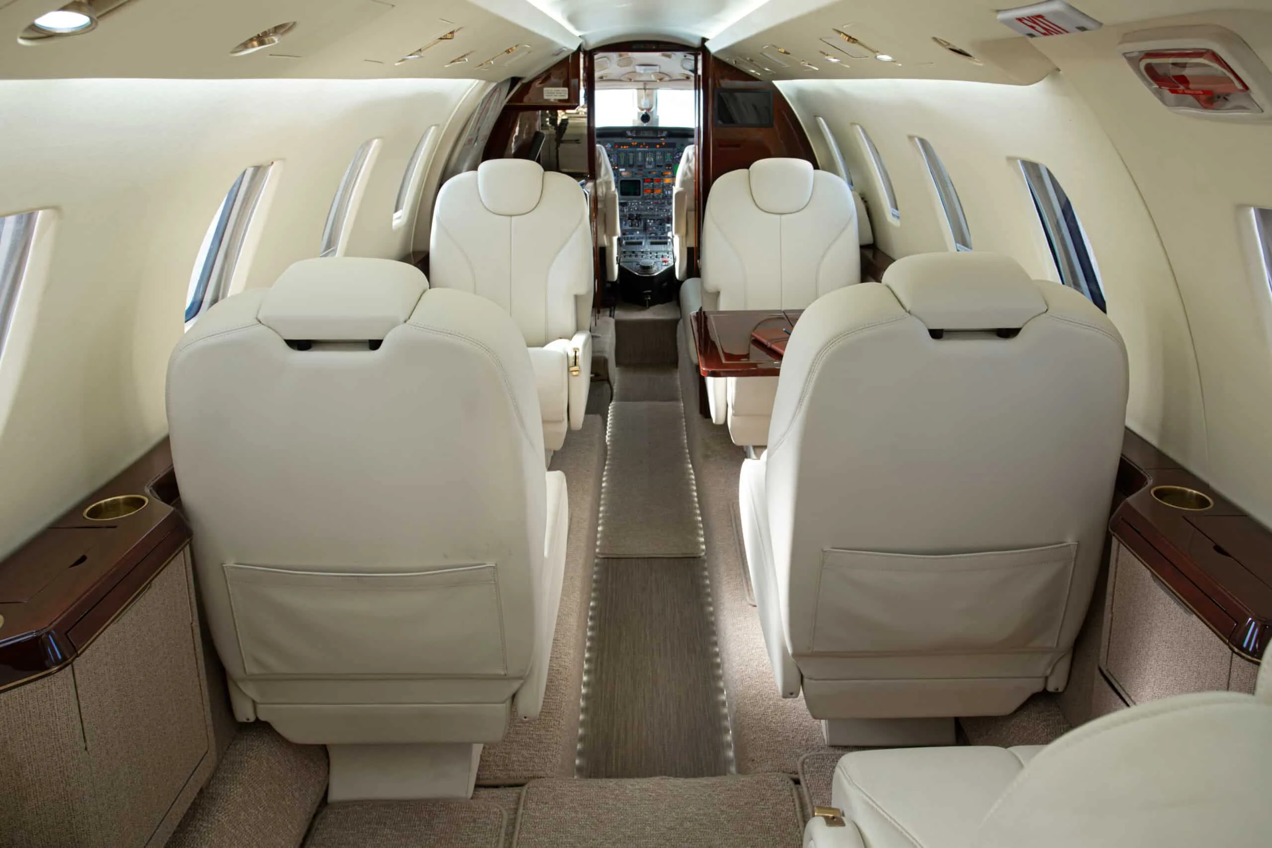 A spacious view of the aircraft cabin with multiple cream leather seats and a central aisle leading towards the cockpit.