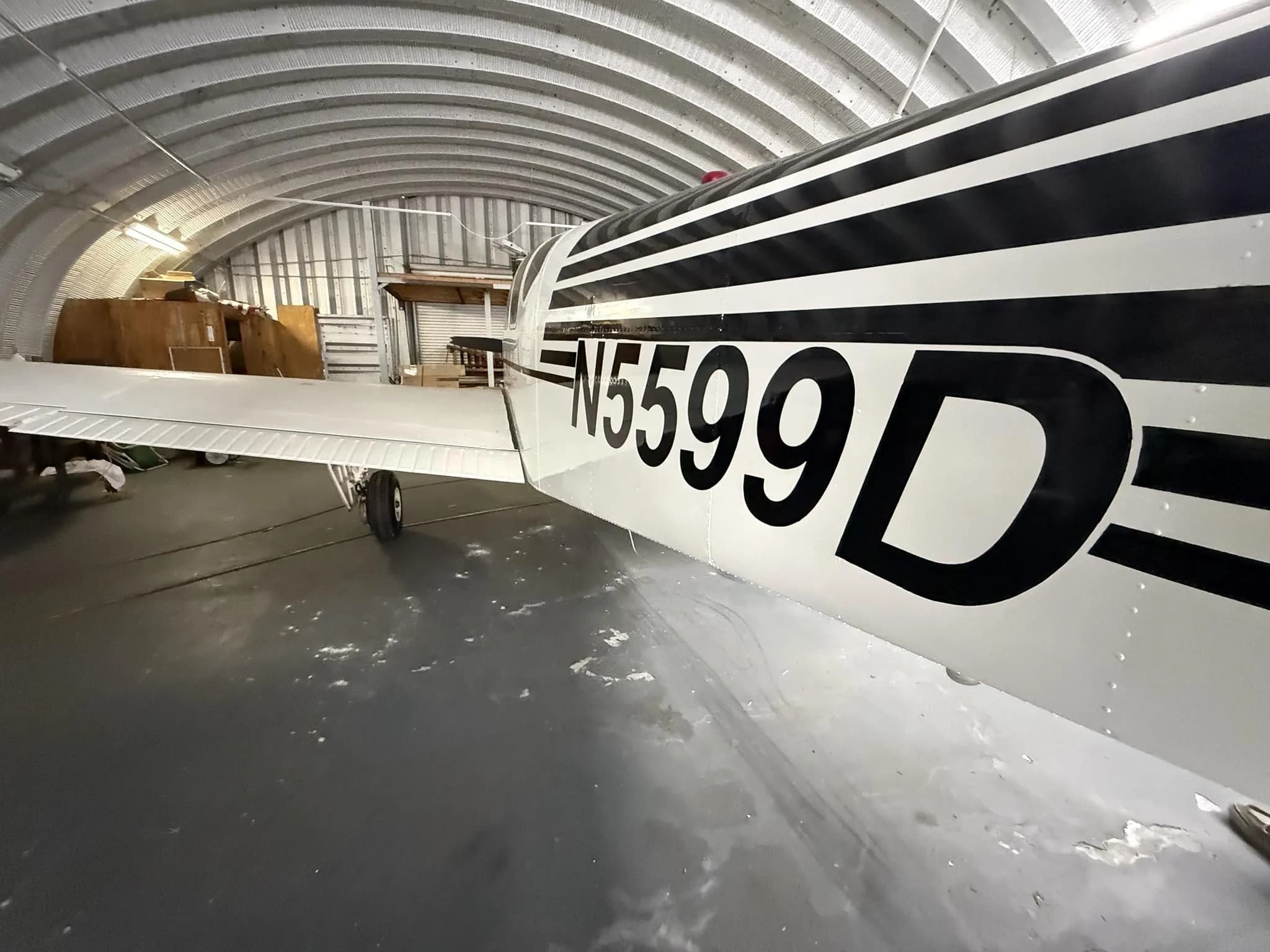 A side view of the white aircraft with black stripes and N5599D registration, parked in a hangar.