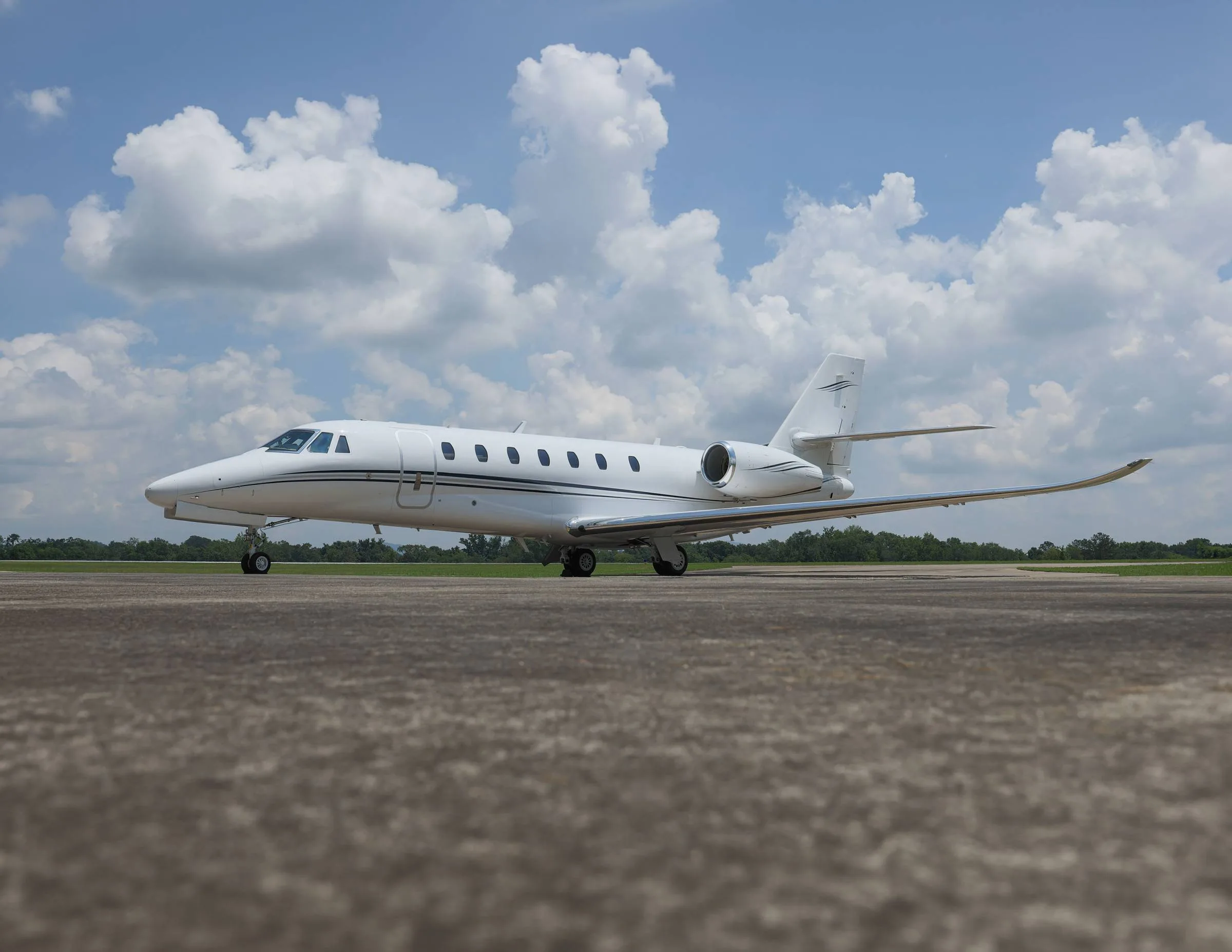 A white business jet with black stripes parked on an asphalt runway under a partly cloudy sky.