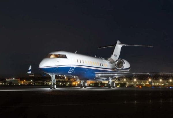 A Bombardier Challenger 300 aircraft is parked on the tarmac at night.