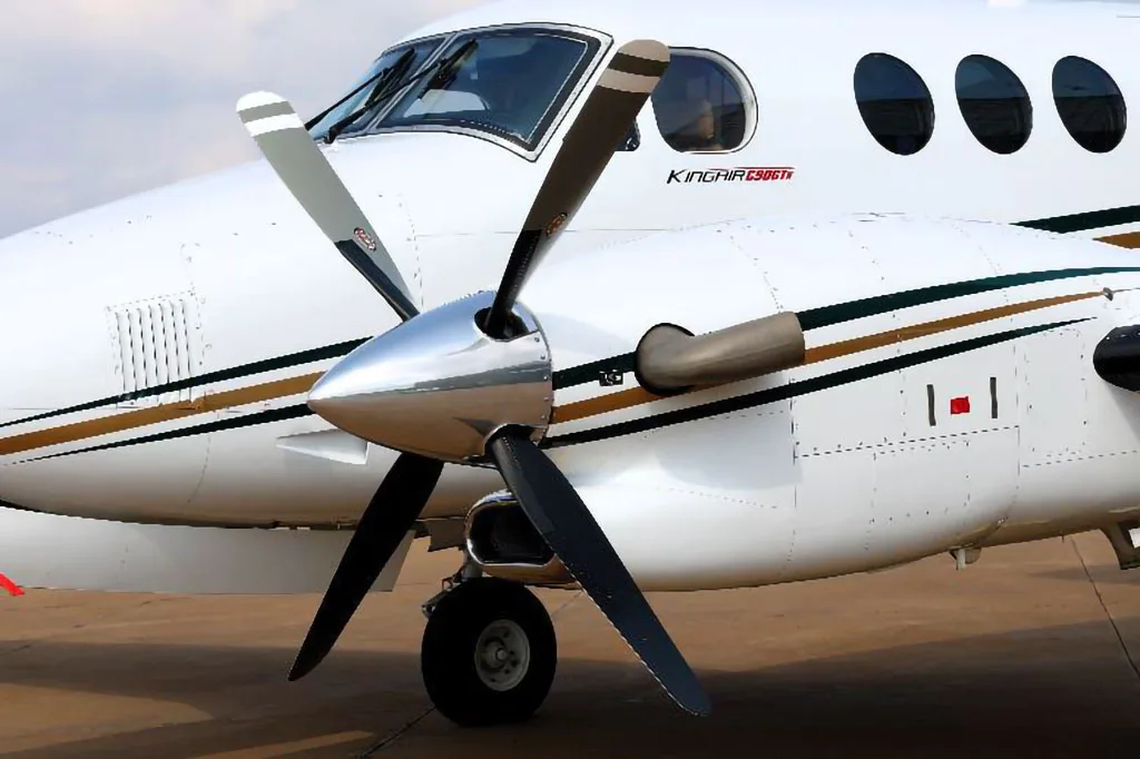 A close-up of the front fuselage and right propeller of a white Beechcraft King Air C90GTx aircraft.