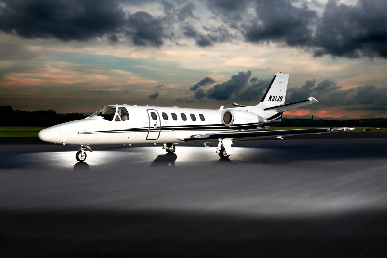 A white Cessna Citation business jet with black stripes, registration N31JB, parked on an airfield at sunset.