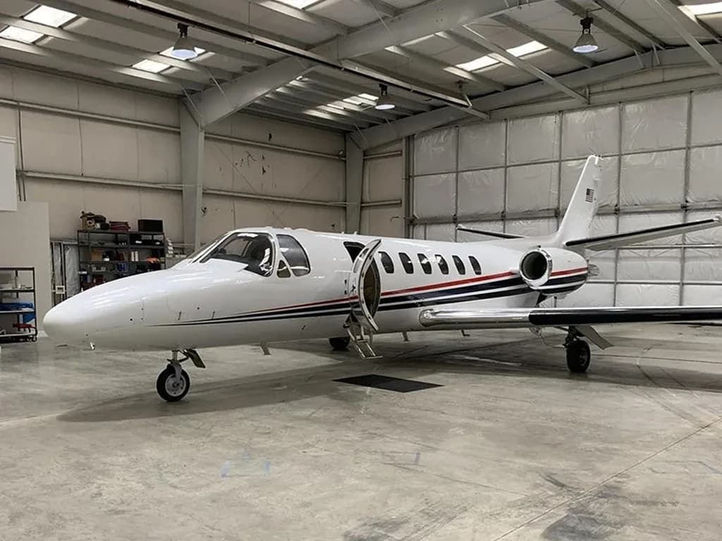 A white business jet with red and blue stripes parked inside a large hangar, with its main door open.