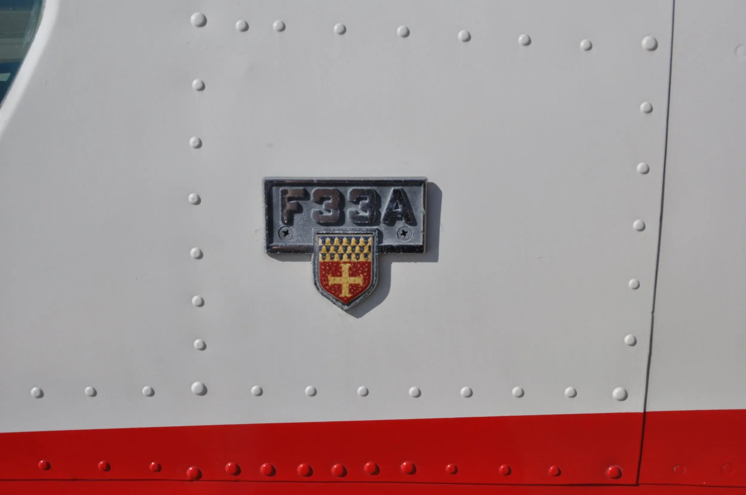A close-up of a metal F33A badge with a crest on the white fuselage of the aircraft.