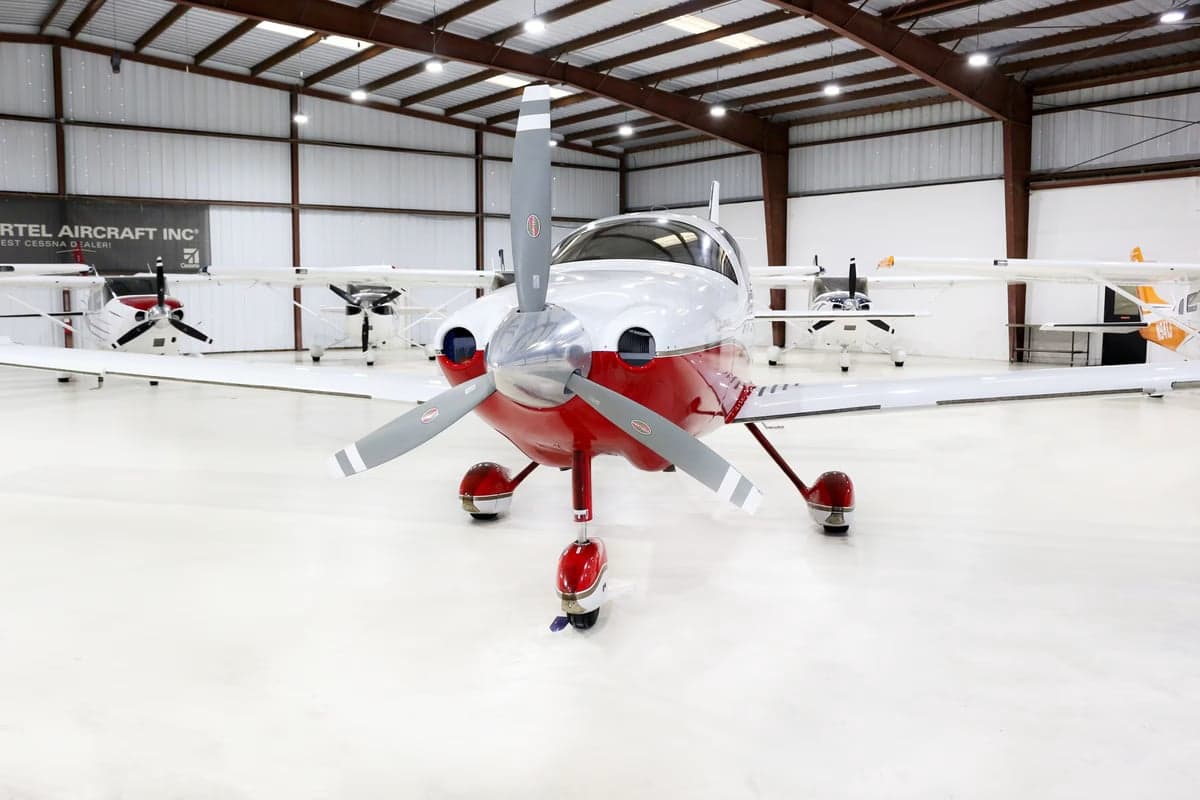 Front view of a Columbia 350 aircraft with red and white paint scheme parked in a hangar.