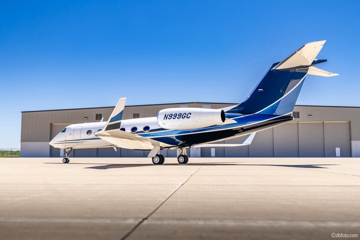 A rear-side view of the N999GC Gulfstream G550 business jet, showcasing its blue and black tail and engine.