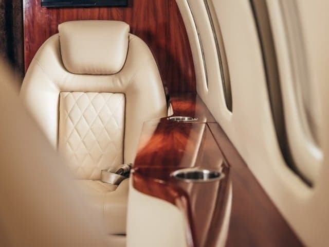 Close-up of a leather aircraft seat with wood trim and cupholders.