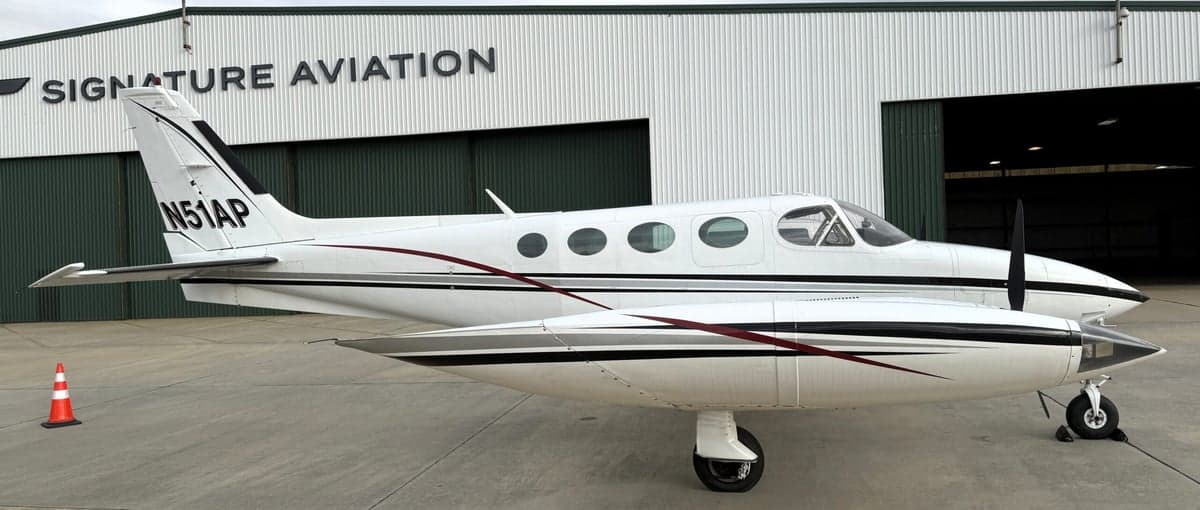 Side view of the Cessna 340A aircraft with registration N51AP parked in front of a Signature Aviation hangar.