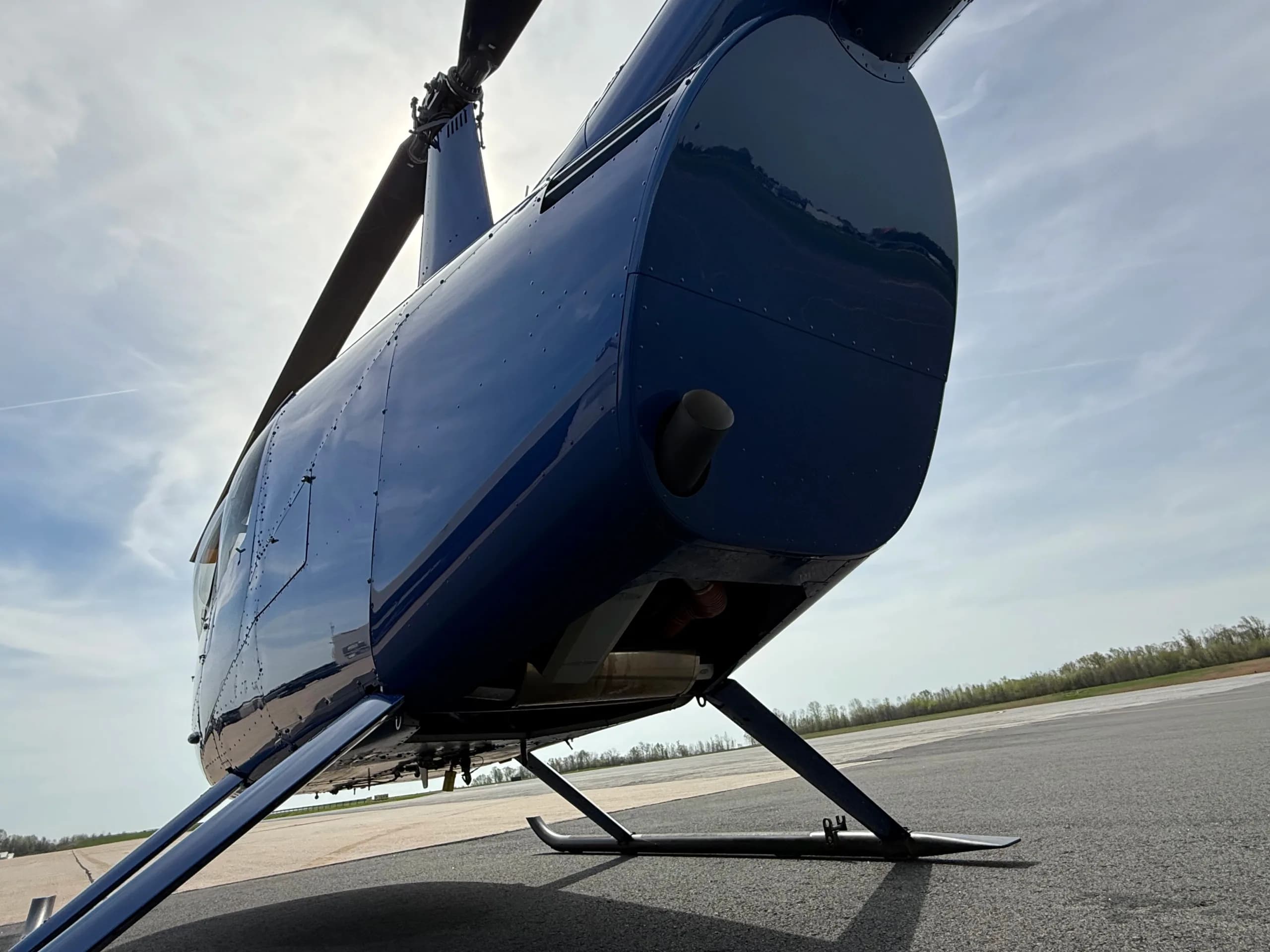 An upward-looking view of the underside of a blue Robinson R44 helicopter fuselage and skid landing gear.