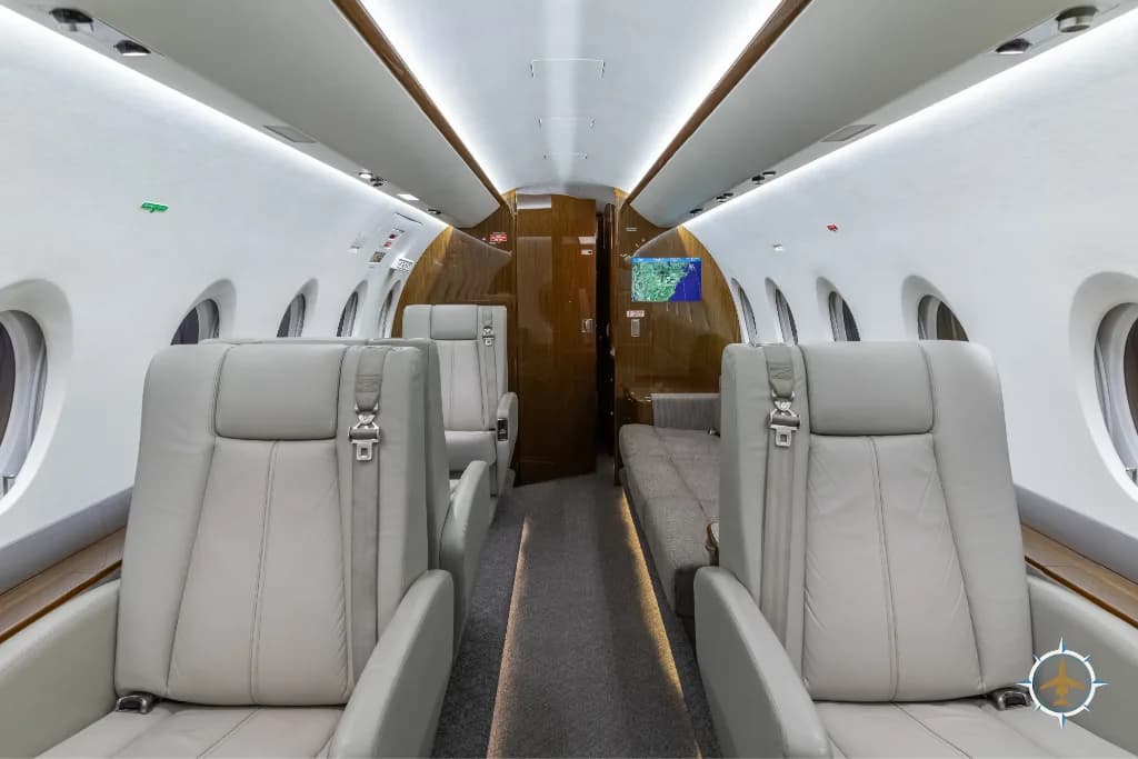 The aircraft cabin interior featuring light grey leather seats and a long sofa on the right side.