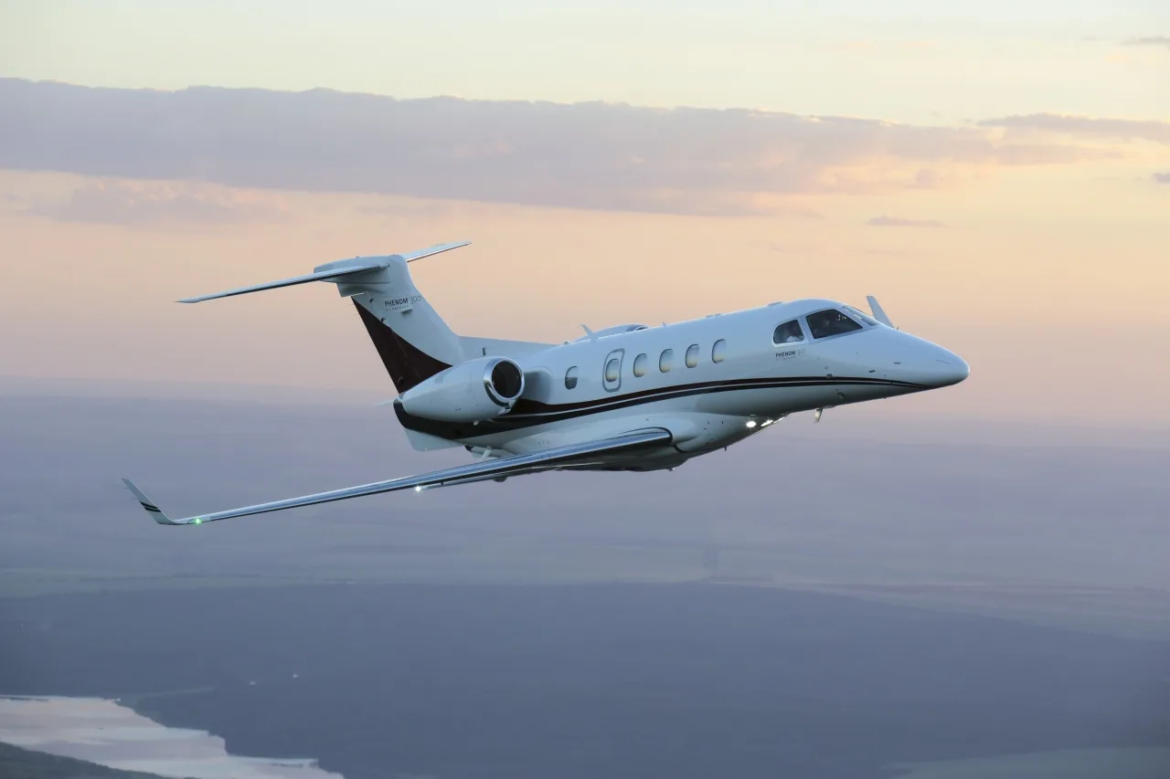 A Phenom 300E in flight against a sunset sky.