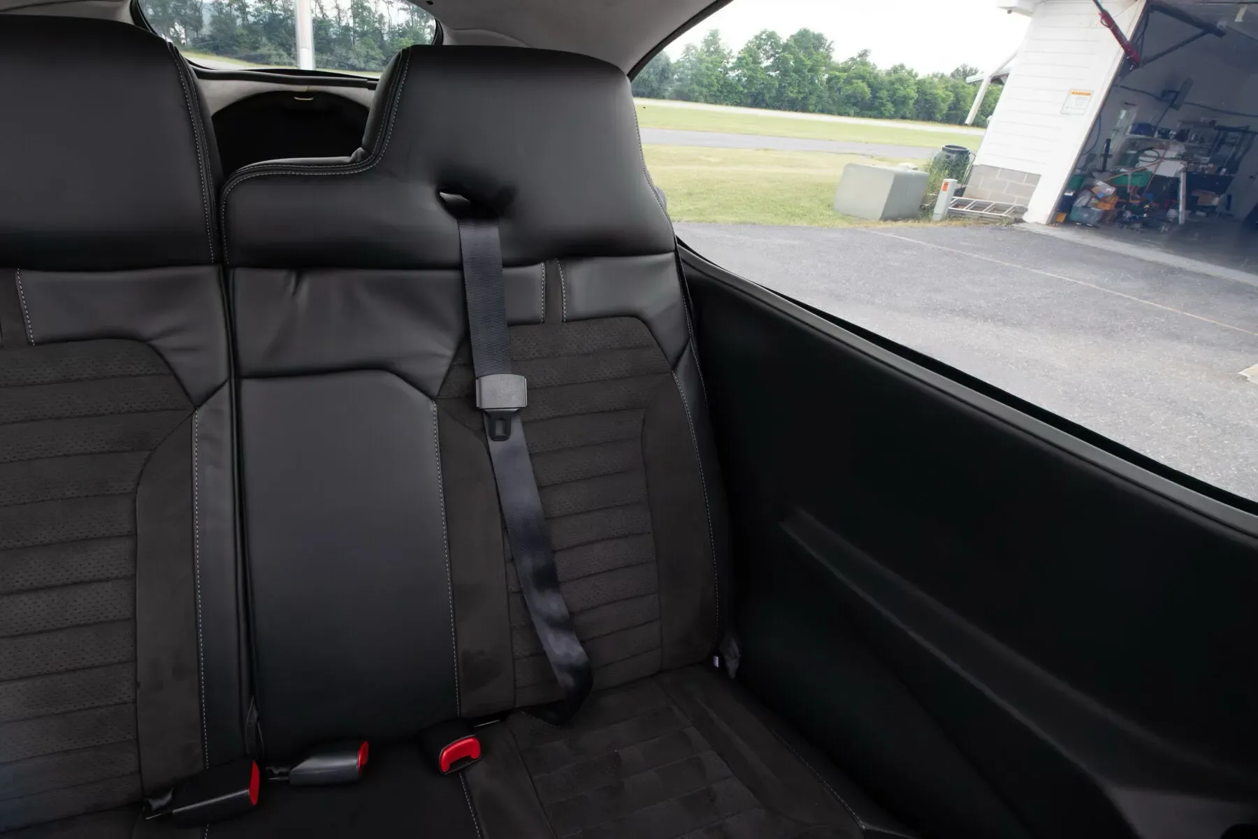 View of the black leather and suede rear seats in the aircraft cabin, looking out the window at a hangar.