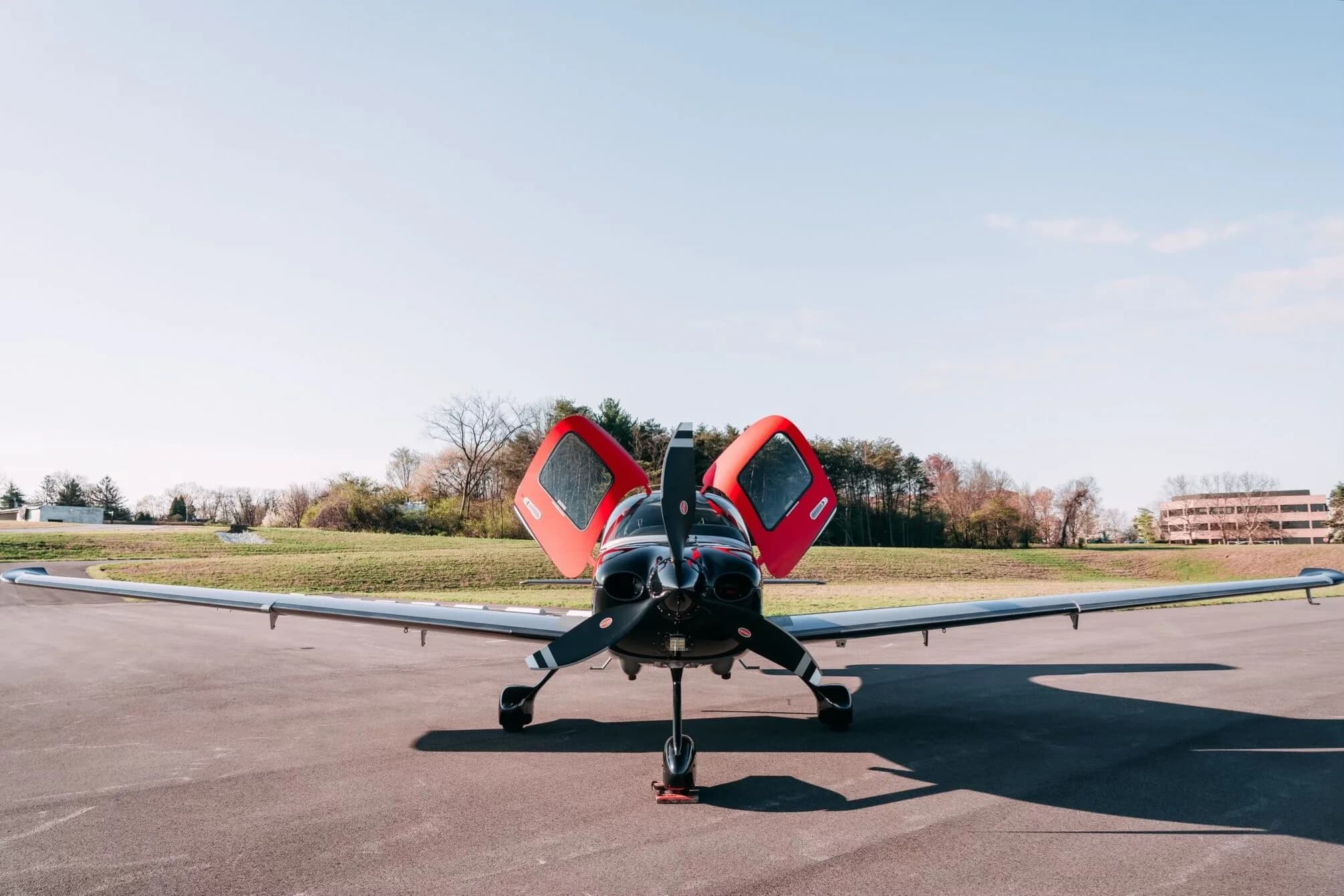 A front view of the red, black, and silver Cirrus SR22T aircraft with its gull-wing doors open.