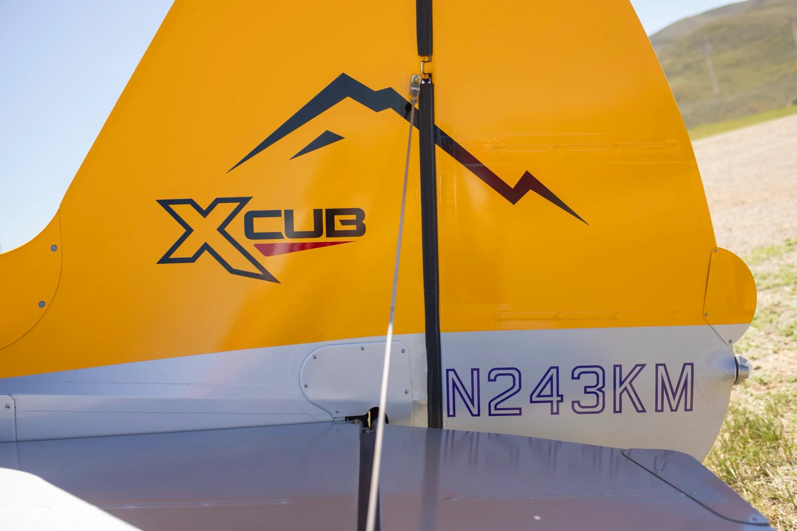 A close-up of the tail of the yellow CubCrafters XCub, showing the "XCUB" logo and registration N243KM.