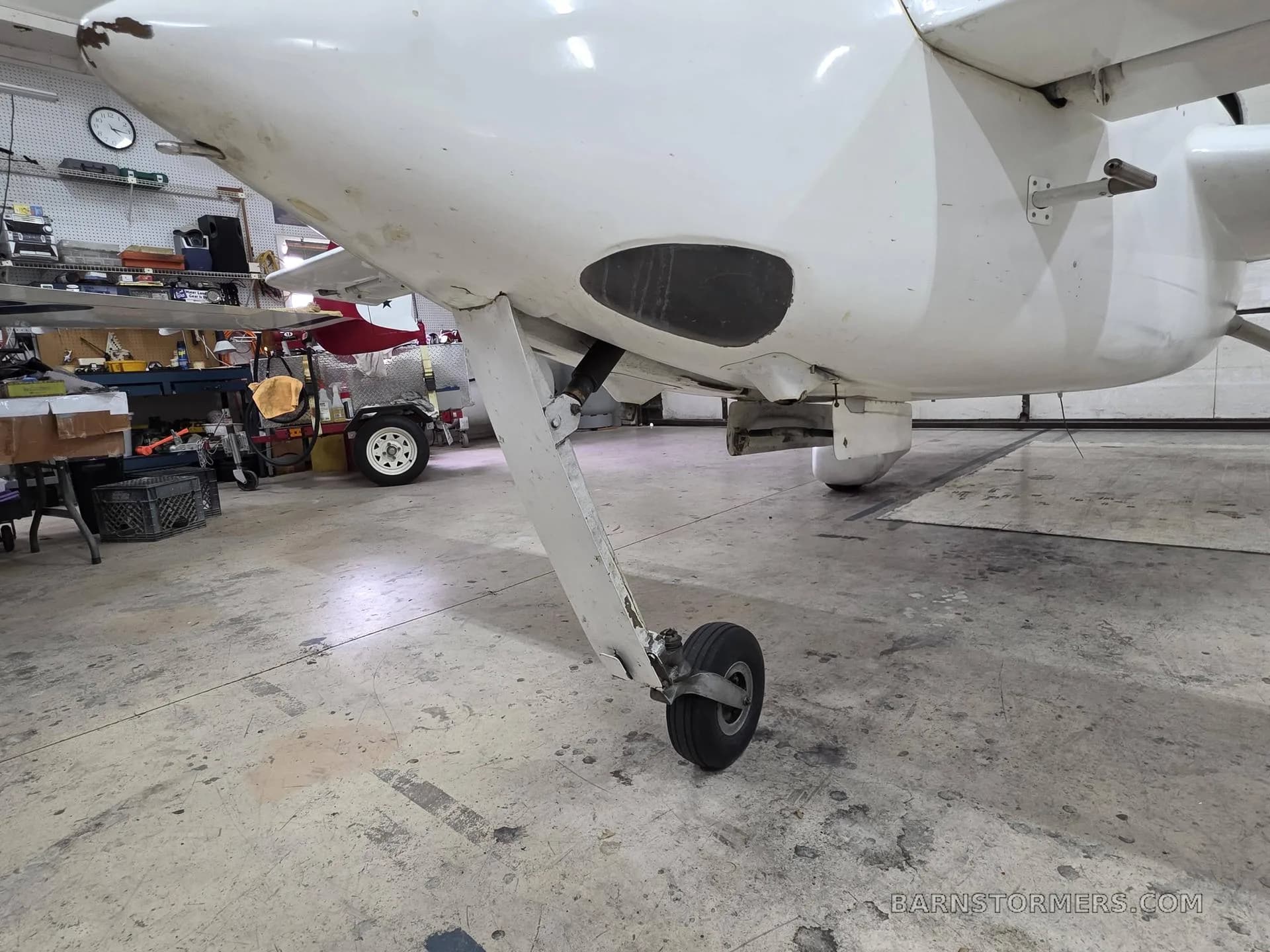 A close-up view of the white experimental aircraft's nose landing gear and underside in a hangar.