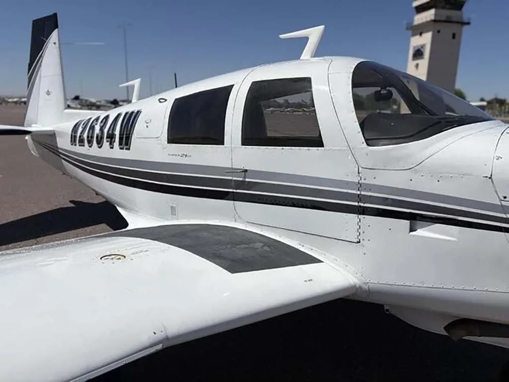 A close-up of the cockpit windows and fuselage of the white Mooney M20 aircraft N2634W.