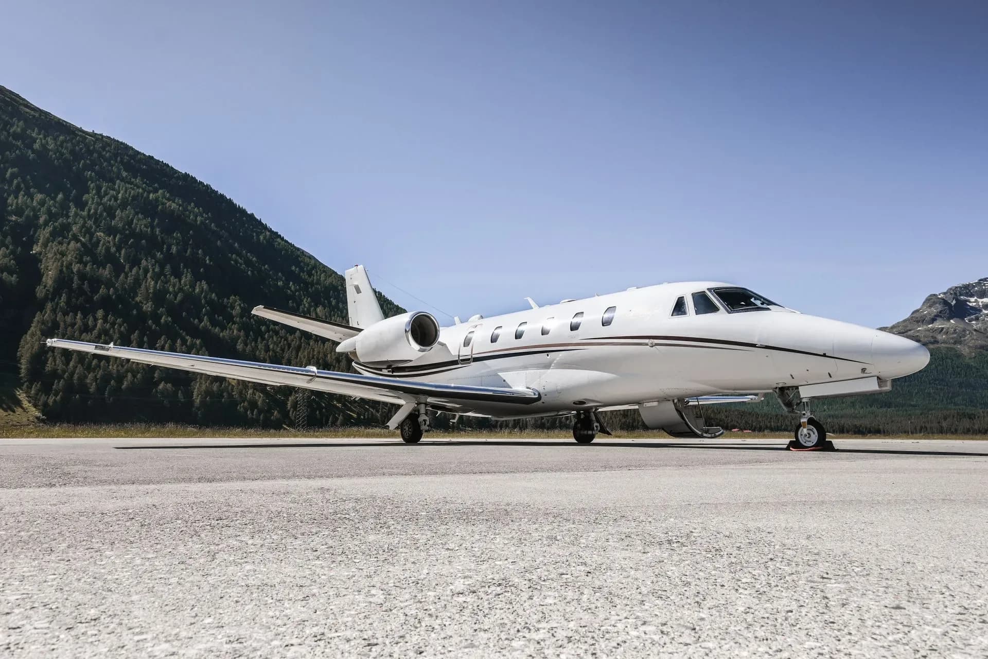 A white business jet is parked on a runway with mountains in the background.