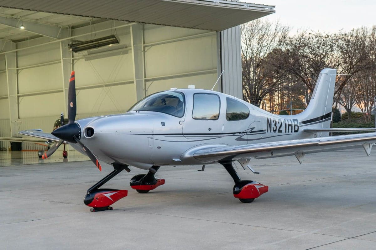 A Cirrus SR22T aircraft with a silver paint scheme parked outside a hangar.