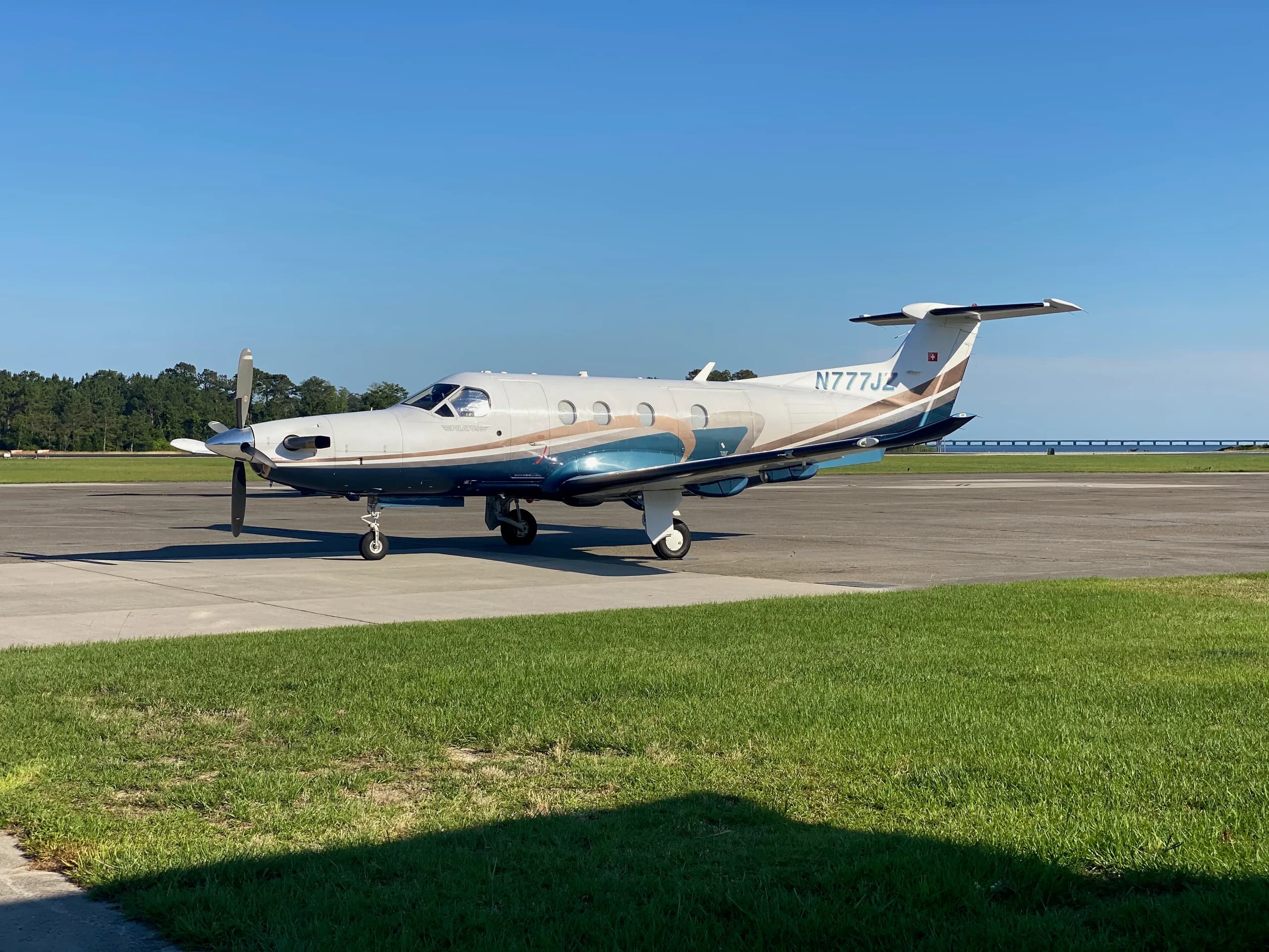A Pilatus PC-12 aircraft with registration N777JZ is parked on the tarmac with a blue and brown paint scheme.