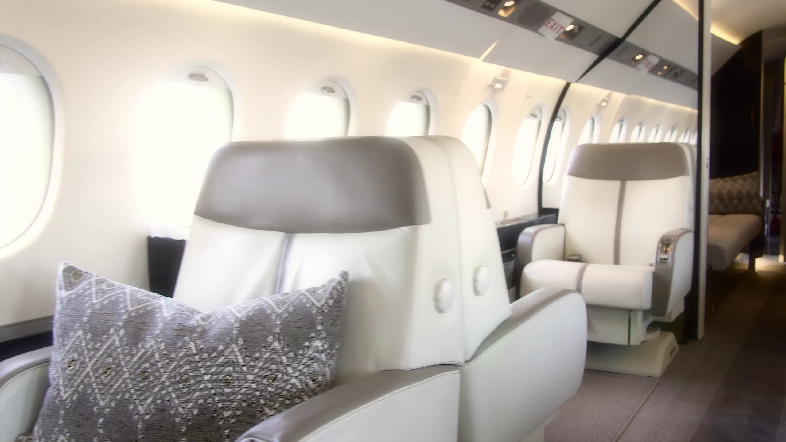 A view down the cabin aisle of a business jet, showing light-colored seats and windows.