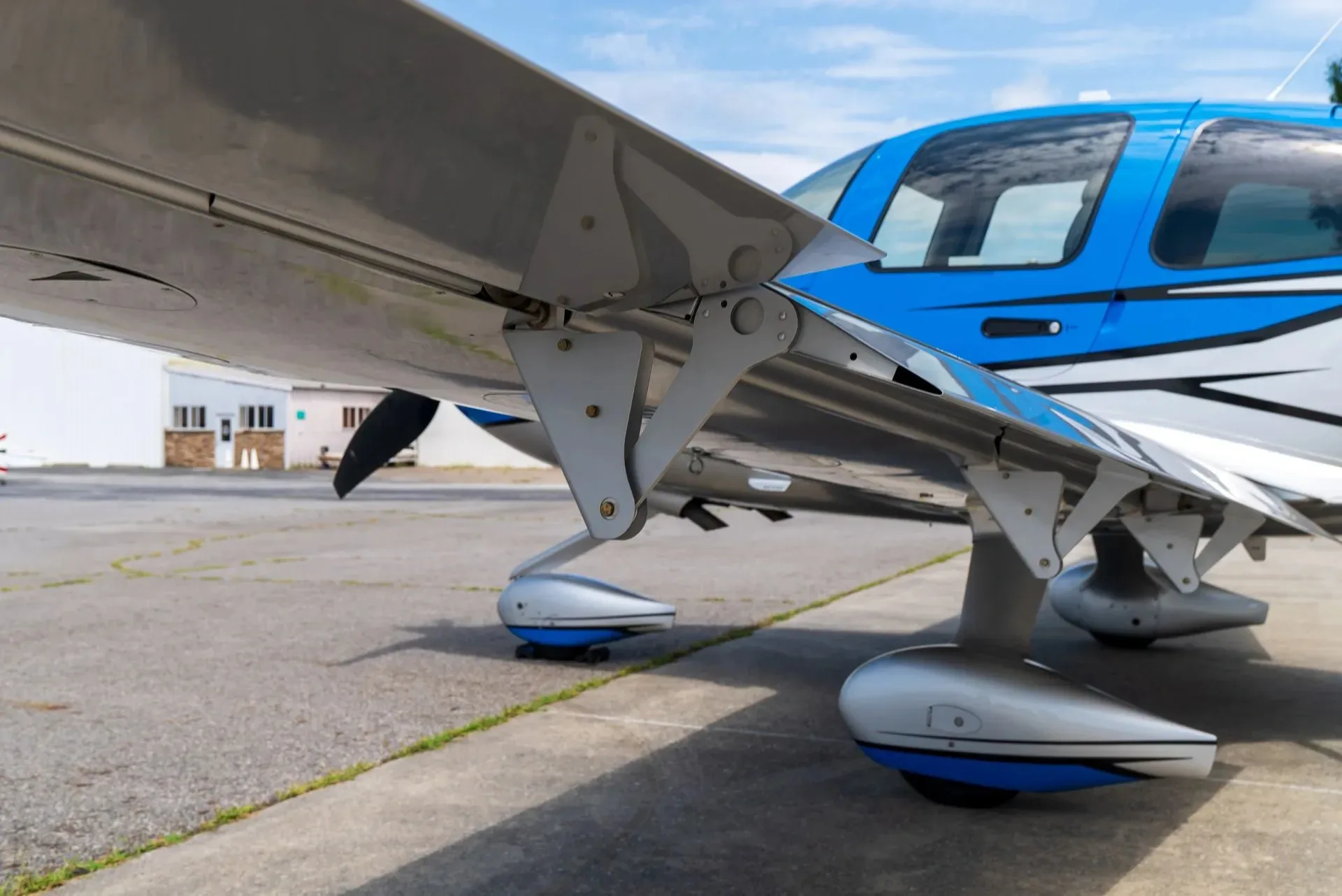 A close-up view of the landing gear and underside of the wing of a blue and silver Cirrus SR22 aircraft.