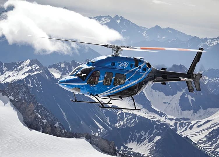 A blue and black Bell 429 helicopter flying over snow-covered mountains.