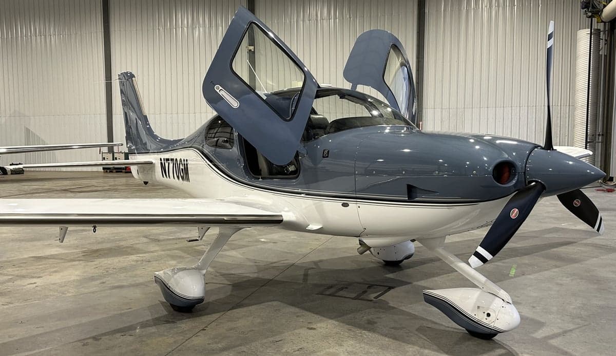 Front view of a gray and white Cirrus SR22 with registration N770GM parked inside a hangar with its doors open.