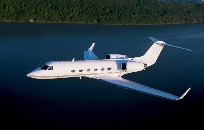 A white Gulfstream jet flies over a lake.