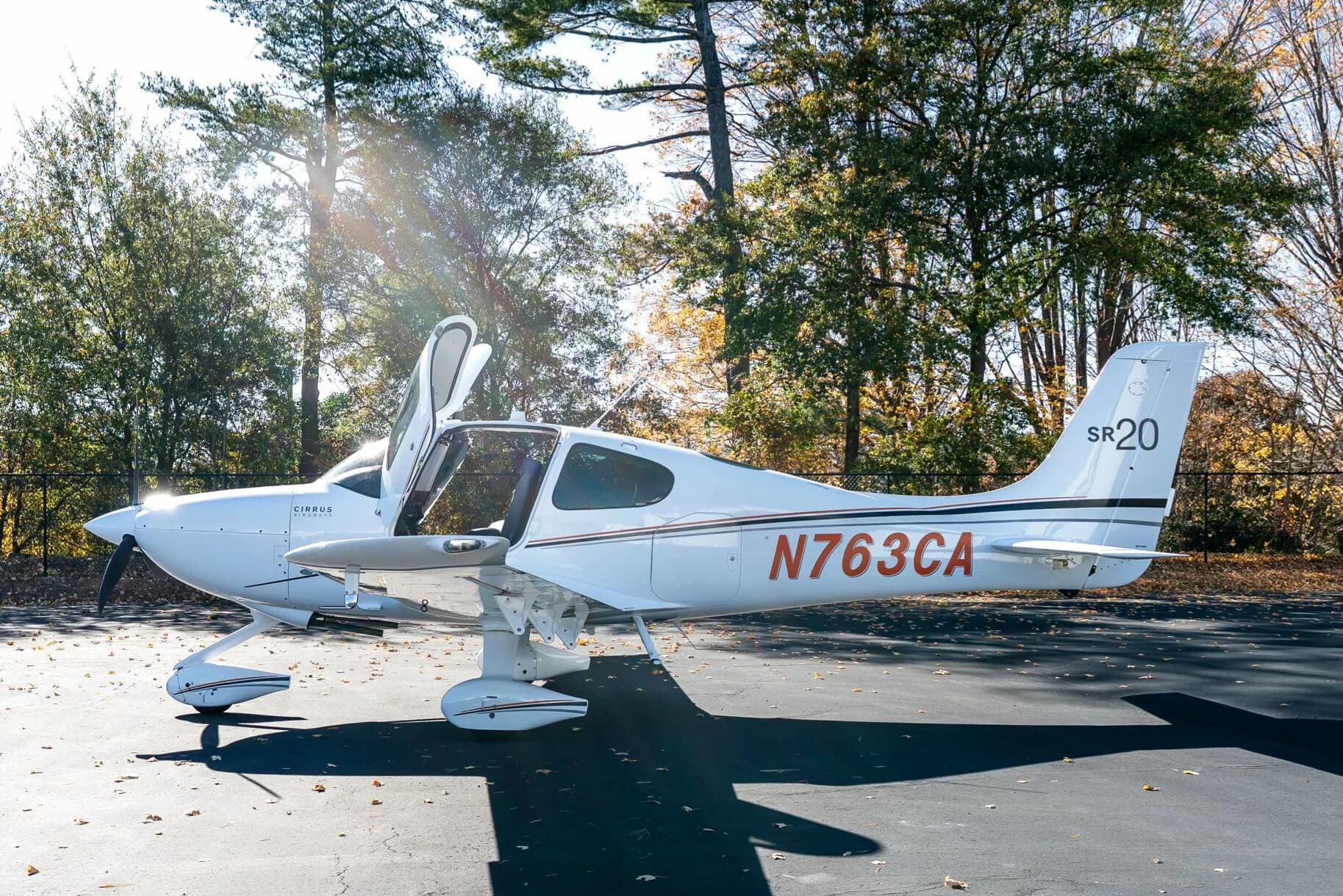 A white Cirrus SR20 aircraft with its doors open is parked on an asphalt tarmac, showing the N-number N763CA.
