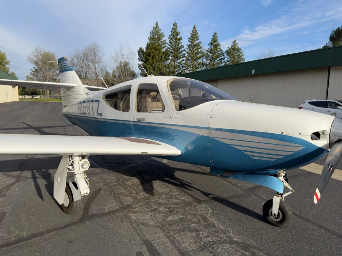 A Commander 114B aircraft with a blue and white paint scheme is parked on the tarmac.