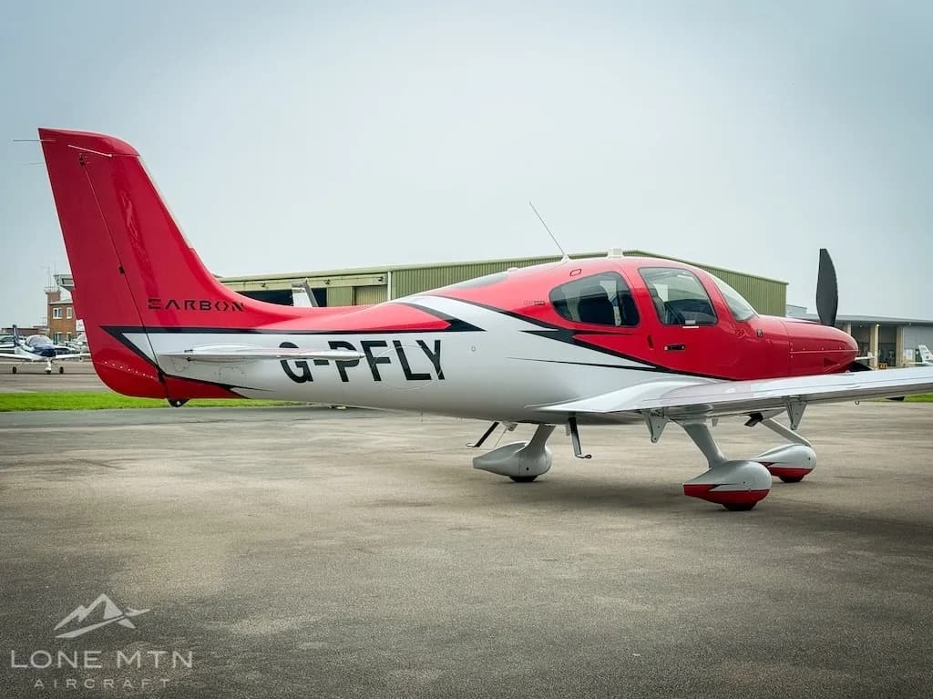 A red and white Cirrus SR22 aircraft (G-PFLY) viewed from the rear-side on a tarmac.