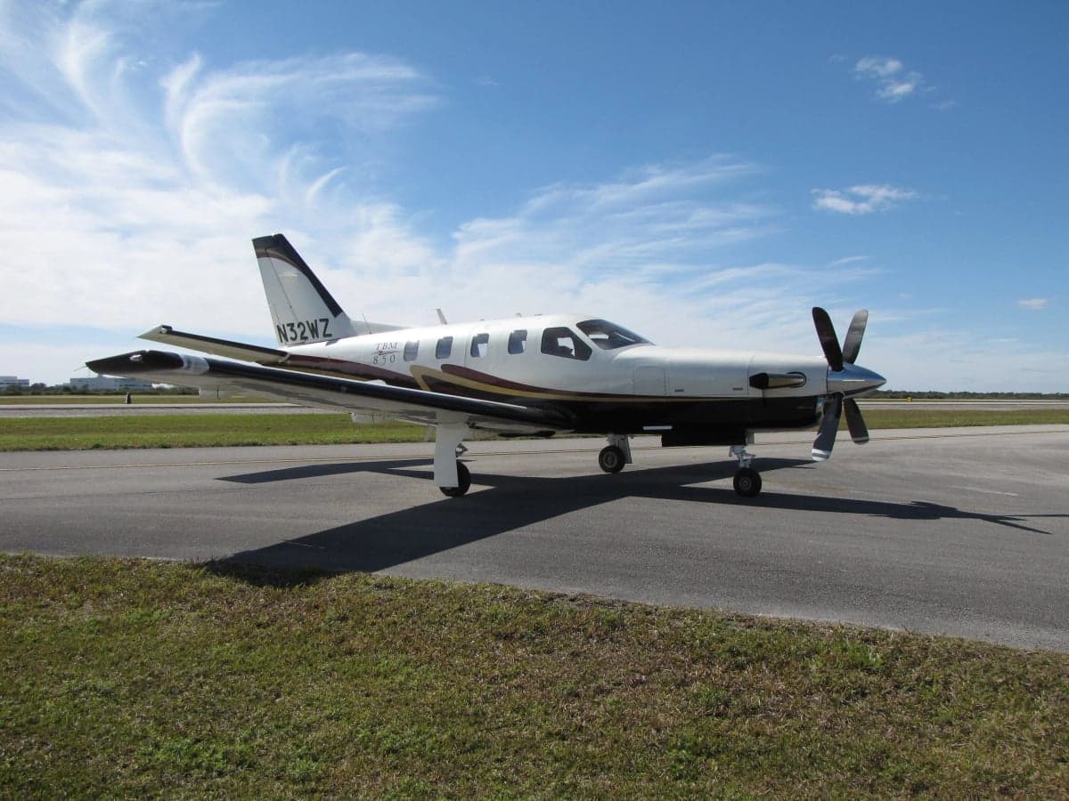 Side view of a TBM 850 aircraft on the tarmac with a white and brown paint scheme.