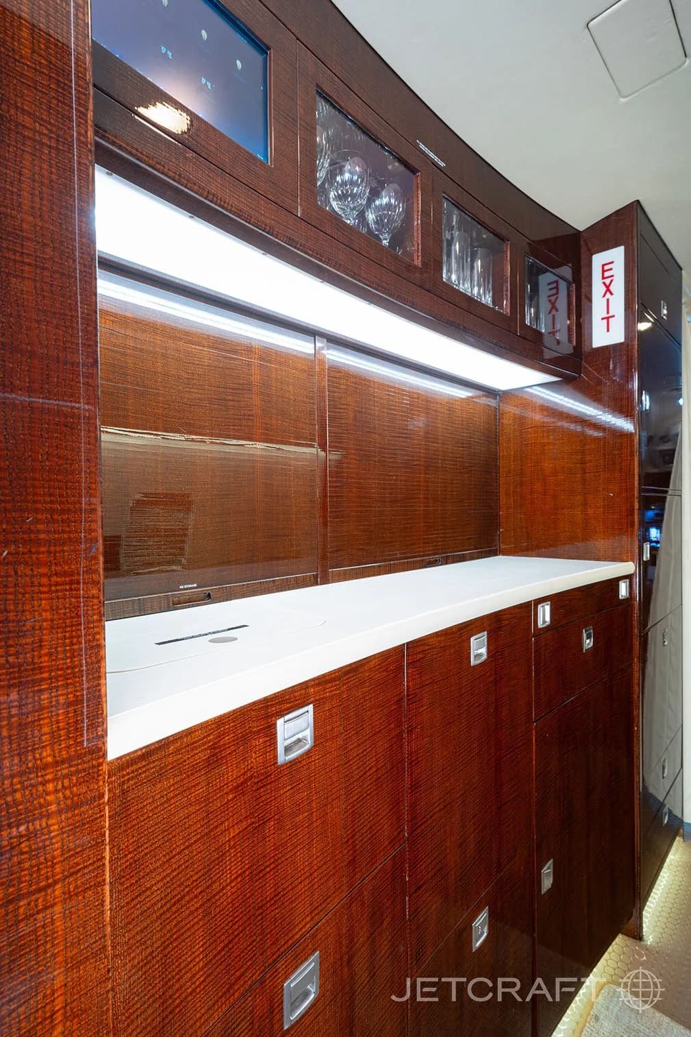 A detailed view of the aircraft's galley area with dark wood cabinets, a white countertop, and glassware.
