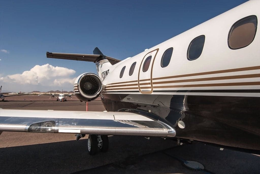 A close-up view of the rear fuselage and engine of the N751MT business jet, showing its black and white paint scheme with gold stripes.