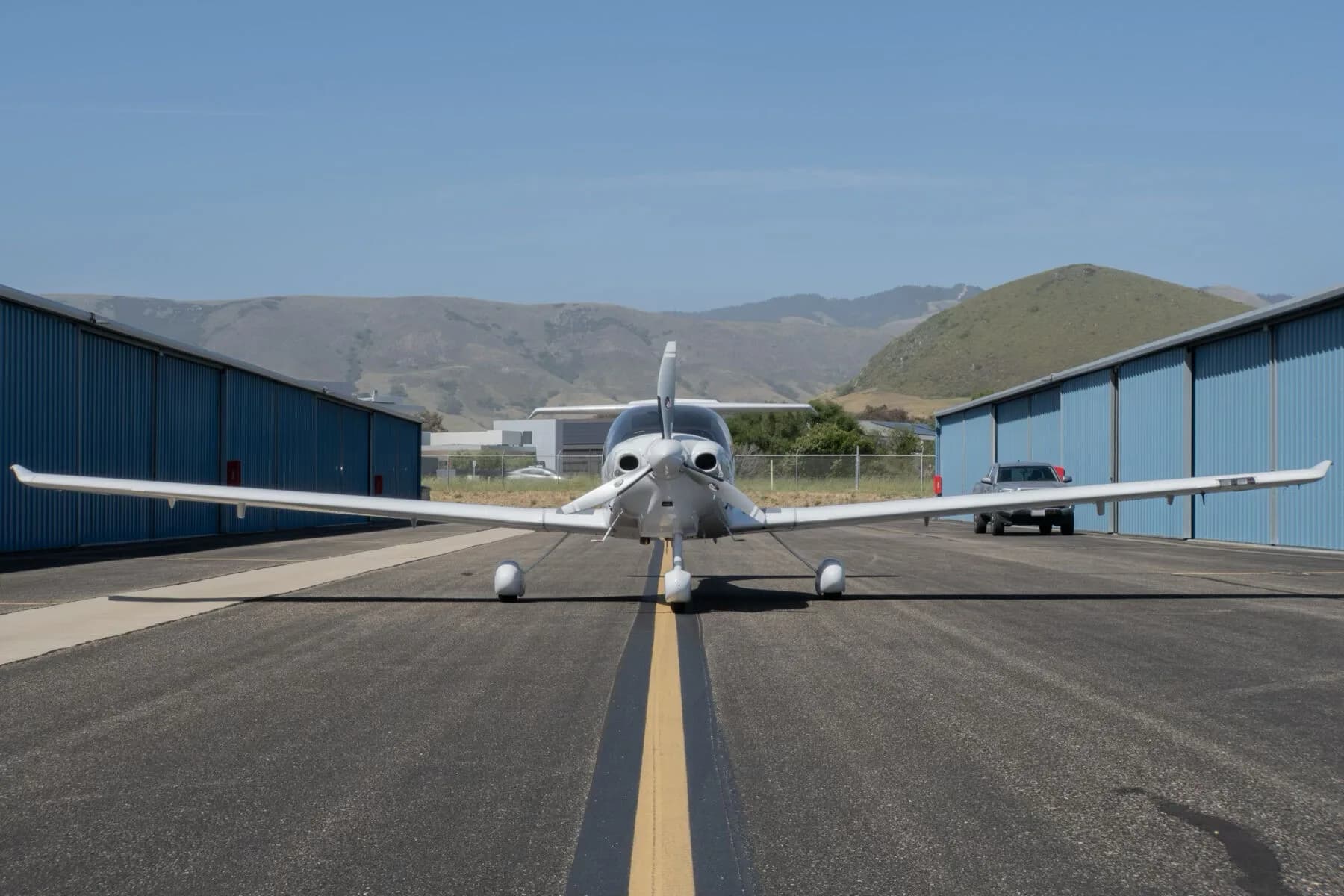 A white Diamond DA40 Star XL aircraft, registration N448US, viewed from the front on an airport runway with hangars and hills in the background.