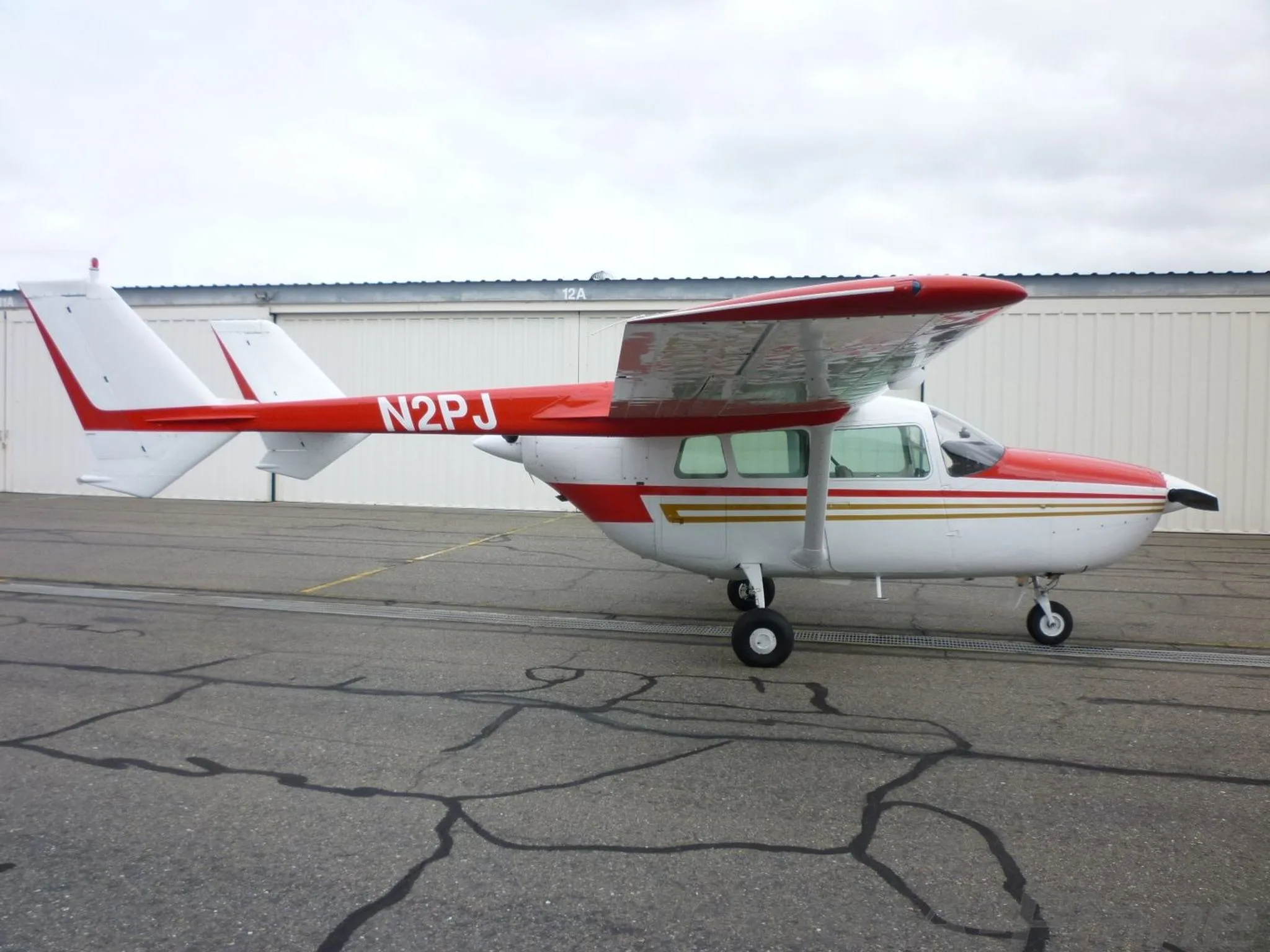 A side view of the white and red Cessna Skymaster N2PJ parked on an asphalt apron.
