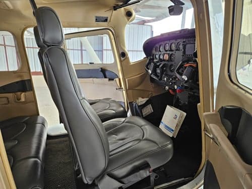 The interior cabin of a Cessna 182 Skylane, featuring gray leather seats and a view towards the cockpit.
