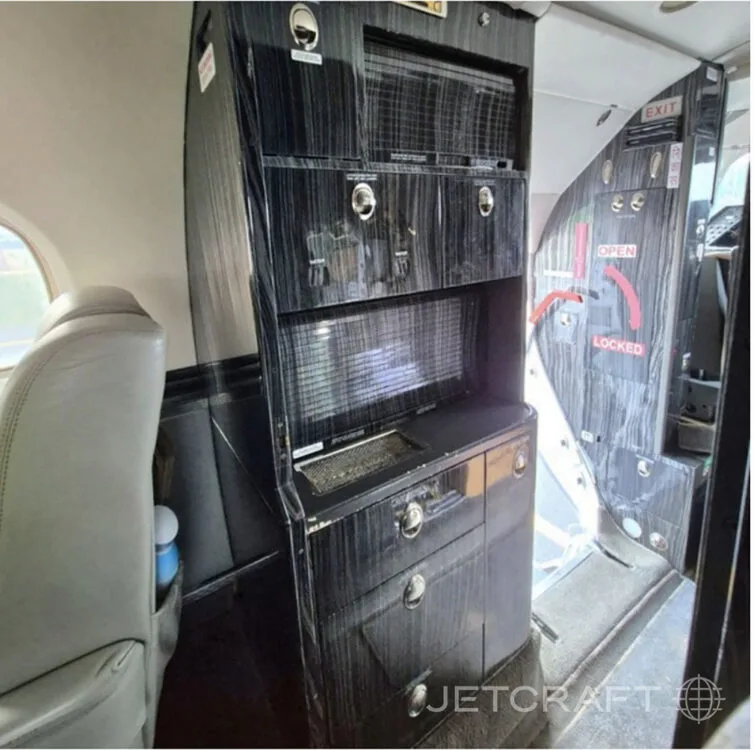 A dark wood-grain galley or storage unit inside a private jet, next to the open entry door.