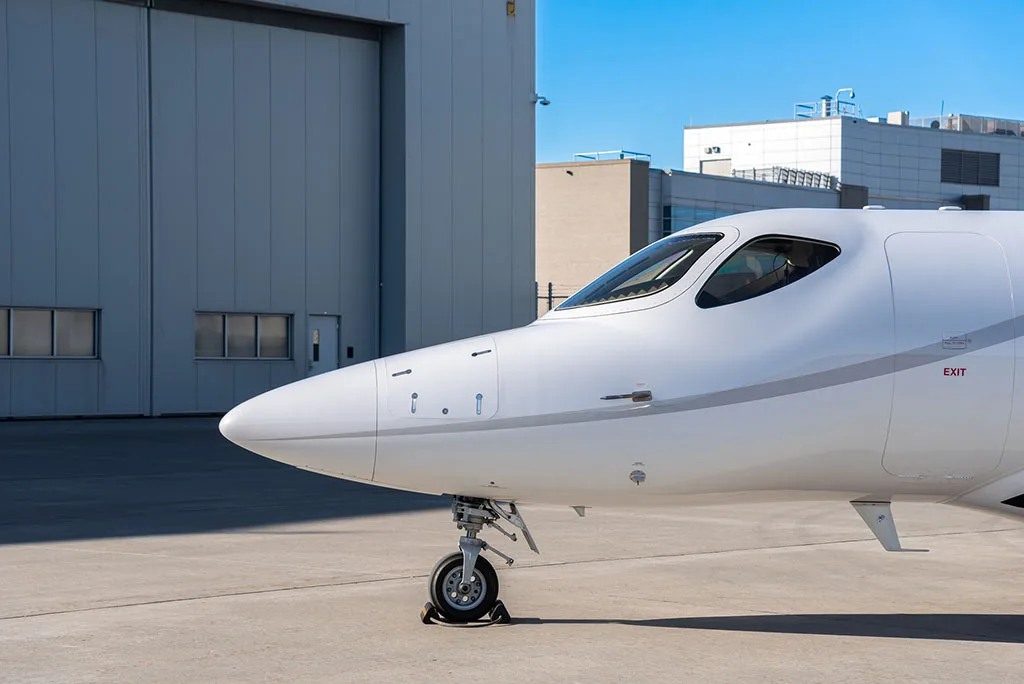 A close-up view of the nose and front landing gear of a white HondaJet HA-420 business jet on a tarmac.