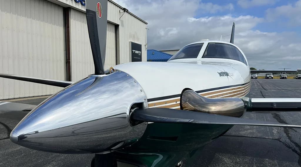 A close-up view of the polished propeller and nose of a white and dark green turboprop aircraft.