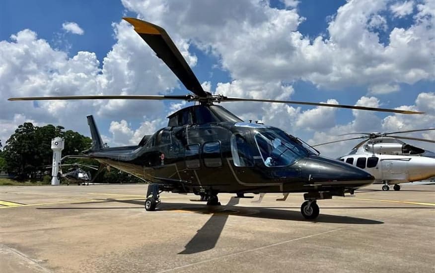 A black helicopter sits on the tarmac under a cloudy sky.