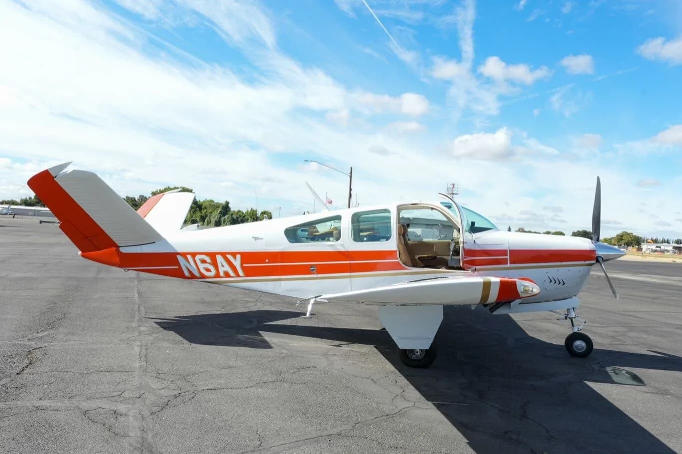 The white and orange Beechcraft Bonanza N6AY with its passenger door open on the tarmac.