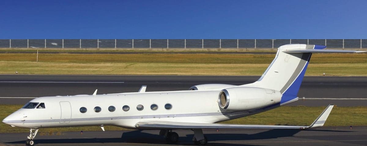 A Gulfstream G550 aircraft is parked on the tarmac with a blue sky overhead.