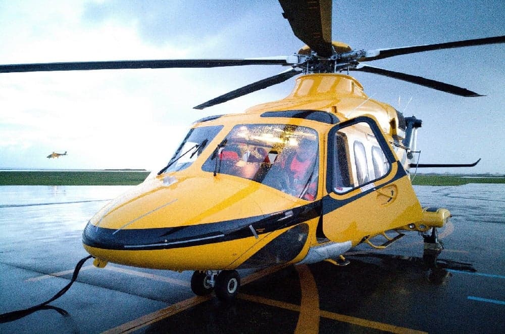 A yellow and black helicopter parked on a wet tarmac.