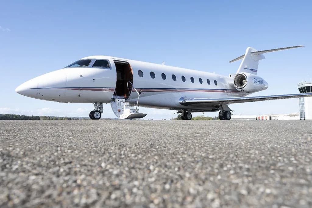 A white business jet with its main door open and stairs extended, parked on an asphalt tarmac.