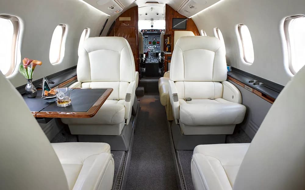 The private jet cabin interior with cream leather seats and a view into the cockpit.