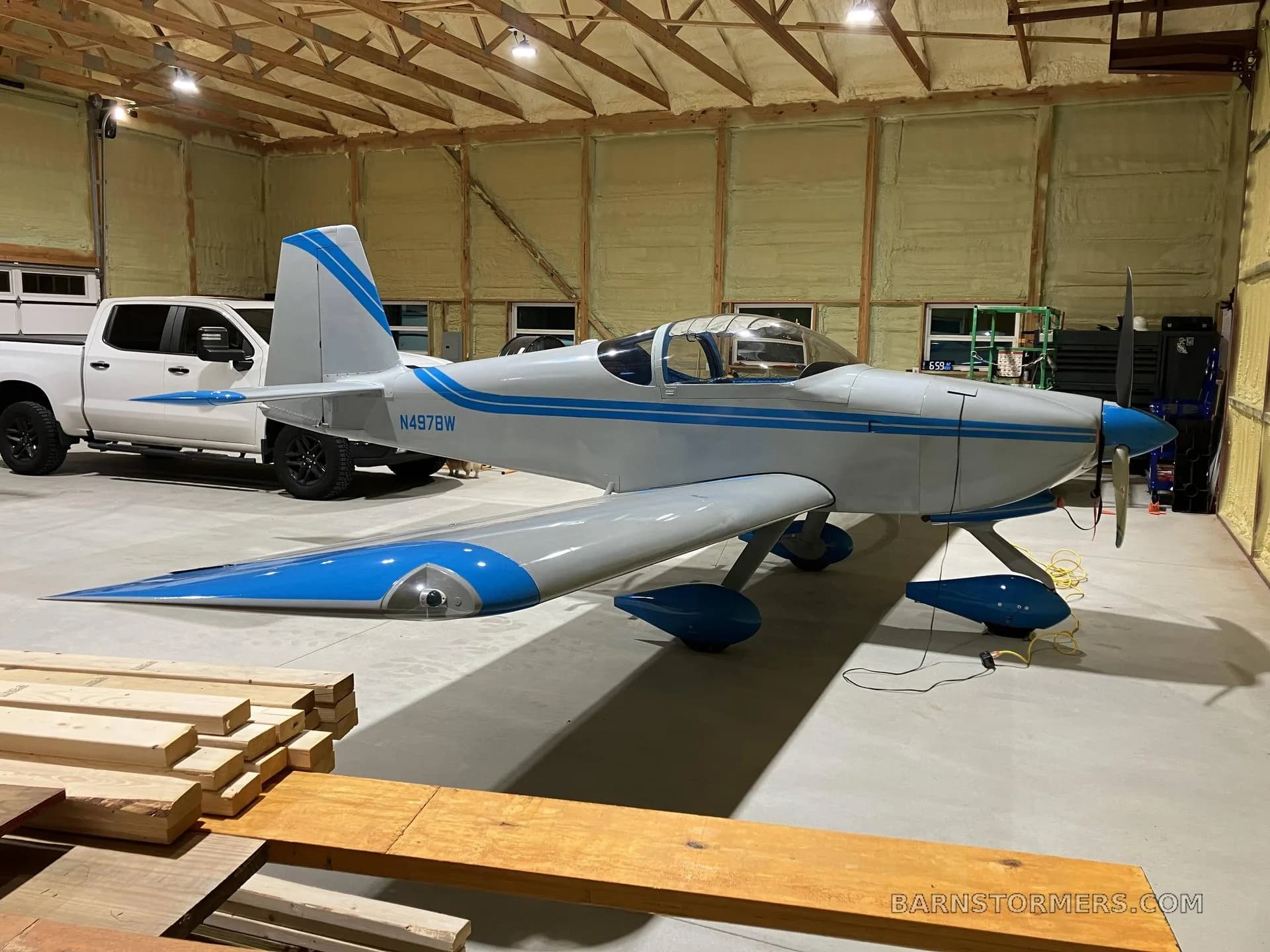 A light gray and blue experimental aircraft, N497BW, parked in a hangar next to a white pickup truck.